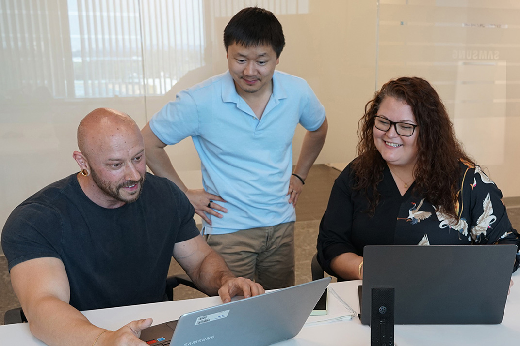 A diverse creative team laughing and collaborating around a table with sketches, color swatches, and laptops